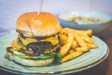 Kızarmış ızgara sığır köftesi (120gm) karamelize soğan, hafif çedar peyniri, romaine marul, dereotu cips ve ot domates sosu ile Brioche Topuz Ile Klasik Burger