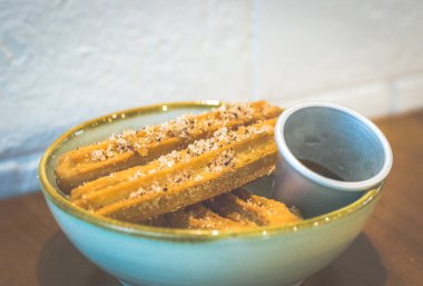 dört churros yığılmış ve şeker ile serpilmiş ve bir kase çikolata sosu daldırma ile servis