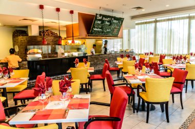 Açık mutfağı olan bir restoranda renkli masalar ve sandalyeler.