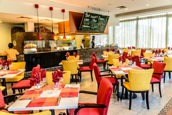 Açık mutfağı olan bir restoranda renkli masalar ve sandalyeler.