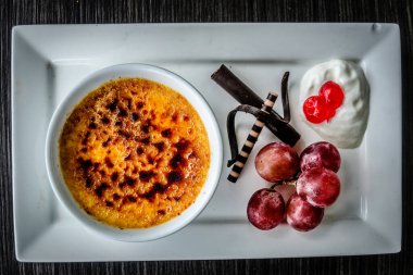 Creme brulee taze krema, tatlı kiraz, çikolata ve üzümle servis edilir.