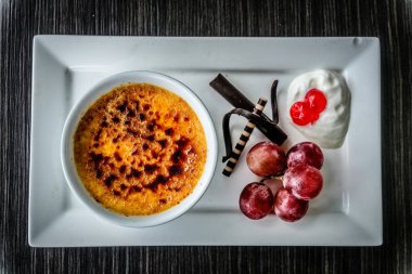 Creme brulee taze krema, tatlı kiraz, çikolata ve üzümle servis edilir.