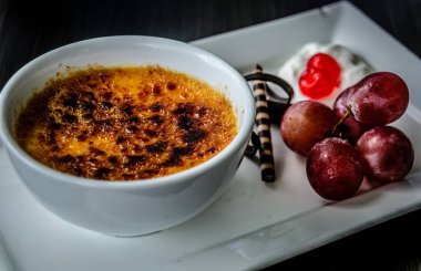 Creme brulee taze krema, tatlı kiraz, çikolata ve üzümle servis edilir.