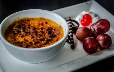Creme brulee taze krema, tatlı kiraz, çikolata ve üzümle servis edilir.