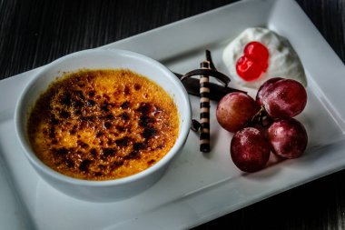 Creme brulee taze krema, tatlı kiraz, çikolata ve üzümle servis edilir.