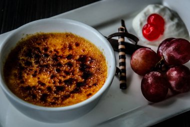 Creme brulee taze krema, tatlı kiraz, çikolata ve üzümle servis edilir.