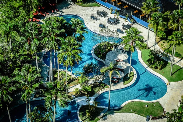 Bella piscina all'aperto circondata da alberi di cocco tropicali, sedie a sdraio, ombrelloni cabana — Foto Stock