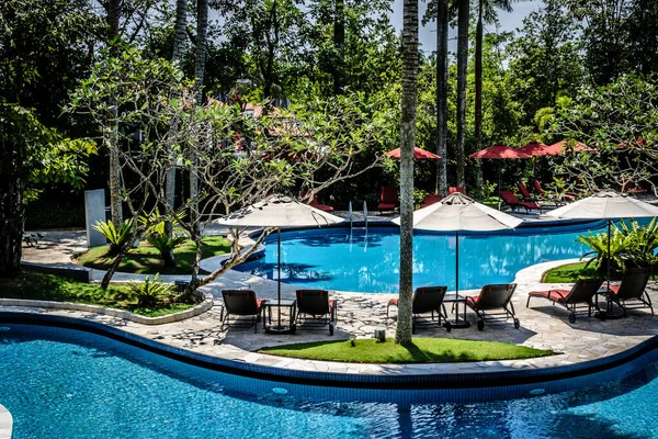 Hermosa piscina al aire libre rodeada de cocoteros tropicales, tumbonas, sombrillas cabaña — Foto de Stock