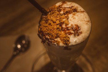 Üzerine tiramisu keki, çikolata sosu, çırpılmış krema ve spekülasyon bisküvisi eklenmiş vanilyalı espresso.