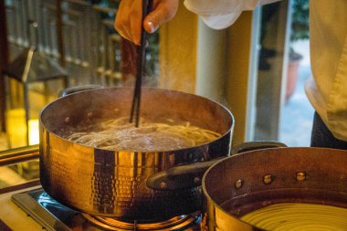 Çinli bir şef Çin eriştesini canlı bir yemek istasyonunda pişiriyor.