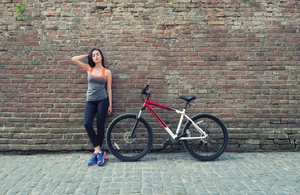 Girl with bike on the wall background. Sport and fitness concept