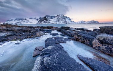 Taşlar ve gün batımı sırasında buz deniz kıyısı. Güzel doğal deniz Lofoten Adaları, Norveç. Deniz ve dağlar, kış