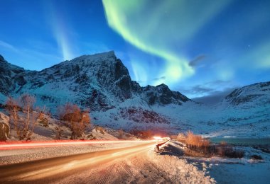 Aurora borealis Lofoten Adaları, Norveç. Yol trafik ve araç hafif bulanıklık. Dağlar yukarıda yeşil Kuzey ışıkları. Kutup ışıkları ile gece gökyüzü. Norveç'te doğal arka plan