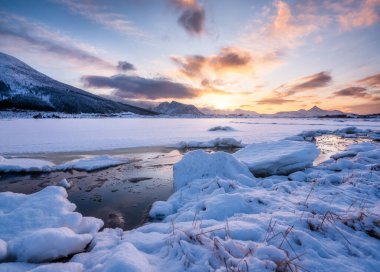 Lofoten Adaları, Norveç. Dağlar, gün batımında karlı ve bulutlu buz. Akşam vakti. Okyanus kıyısındaki kış manzarası. Norveç - seyahat