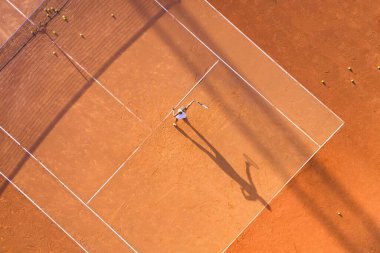 Sağlıklı yaşam tarzı. Genç bir kız kortta tenis oynar. Tenis oyuncusunun havadan görünüşü. Toprak kort. Spor geçmişi. İHA 'dan hava görüntüsü. 