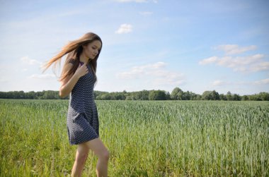 Tahıl alanının yanındaki çayırda yürüyen minyon kadın. Kadın modeli ve doğa.