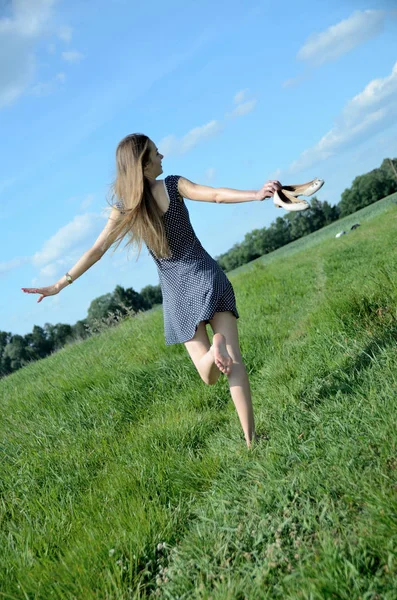 娇小的女人走在草地上 裸脚和鞋子在她的手 女性模式以张开双臂享受自然与自由 — 图库照片