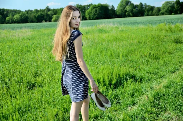 Petite woman walking in the meadow, stepping on grass with bare feet. Female model and nature.