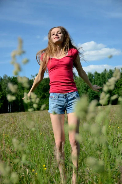 草地上有牛仔裤短裤和红色上衣的女人 女性模型与自然 — 图库照片