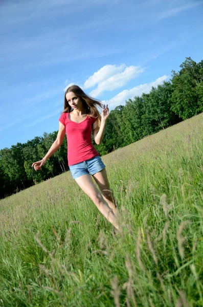 草地上有牛仔裤短裤和红色上衣的女人 女性模型与自然 — 图库照片