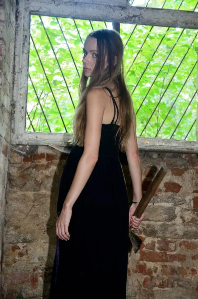 Woman in the ruins holding an ax in her hand. Female model with black dress inside ruins, old palace in Poland.