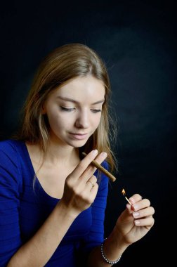 Genç kadın aydınlatan cigarillo ile eşleşir. Siyah arka plan mavi elbiseli kadın.