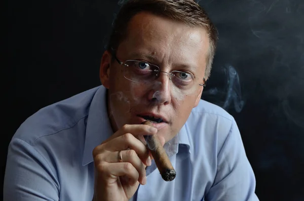 Male model, 35 years old. Man with glasses, wearing light blue shirt, holding cigar in his hand.