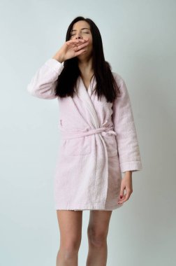 Beyaz arka plan ile sabahlık giyen genç erkek. Sabah kirlenmiş, esneme ve germe. 