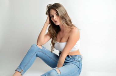 Kot pantolon ve beyaz bluz çekici genç kadın portresi. Yerde oturan kaslı kadın modeli.