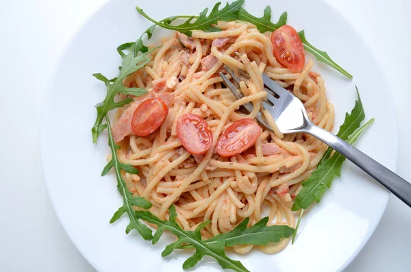 Schurwald jambon, domates sos ve taze argula spagetti. Gümüş çatal ile beyaz tabakta makarna.