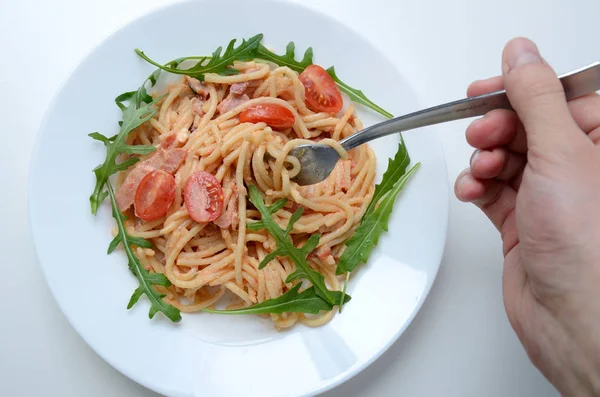 Schurwald jambon, domates sos ve taze argula spagetti. Beyaz tabak, çatal tutan el makarna.