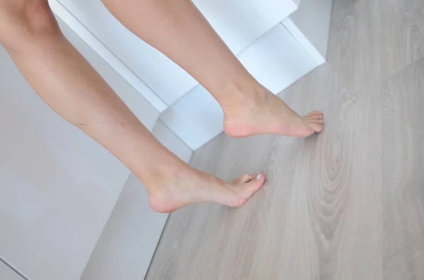 Young woman posing inside apartment. Shapely legs, feet and calf. Both feet on the floor.