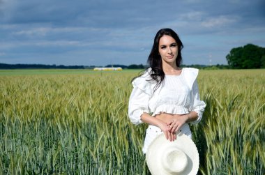 Etrafı arpa tarlasıyla çevrili beyaz şapkalı köylü kızı. Beyaz bluz ve beyaz şort giyen güzel bir esmer.