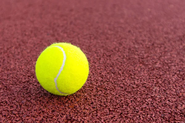 Žlutý tenisový míček na hnědém hřišti — Stock fotografie