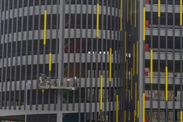 the builder is on the cradle, paints the metal constructions in yellow on the parking facade