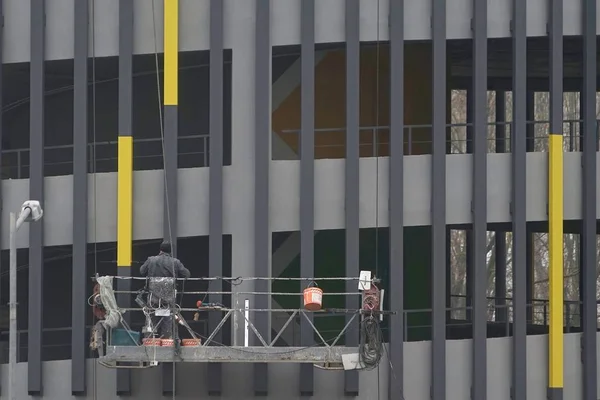 the builder is on the cradle, paints the metal constructions in yellow on the parking facade
