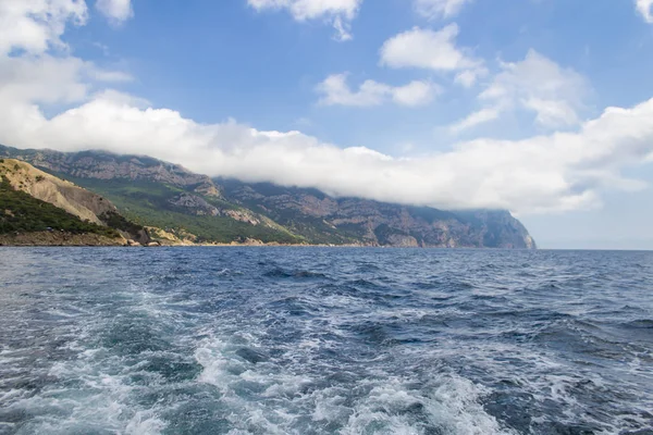 Dağlar ve deniz. Stratus bulutları dağda uzanır. Azgın deniz.