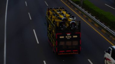 Sarı brandayla kaplı motosikletleri taşıyan bir kamyon otoyolda hareket halinde yakalanıyor ve bulanık bir etki yaratıyor. Otoyol trafiğini, nakliyeyi ve ticari araç hareketini resmediyor