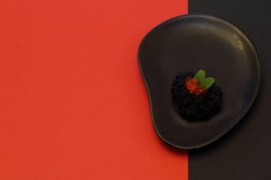 Siyah ve kırmızı. SterIeti siyah tuzlu havyar Kırmızı somon havyar ile dekore edilmiş ve zıt siyah ve kırmızı arka plan ile alışılmadık şekli siyah seramik levhasında nane yaprakları. Minimalizm tarzı