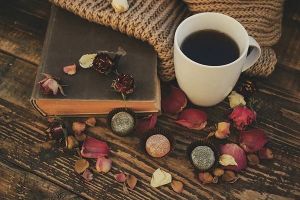 A mug of tea and a book surrounded by dry flowers and candy.