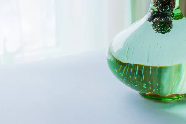 Carbonated drink with blackberries in a glass transparent green decanter on a light background close-up.