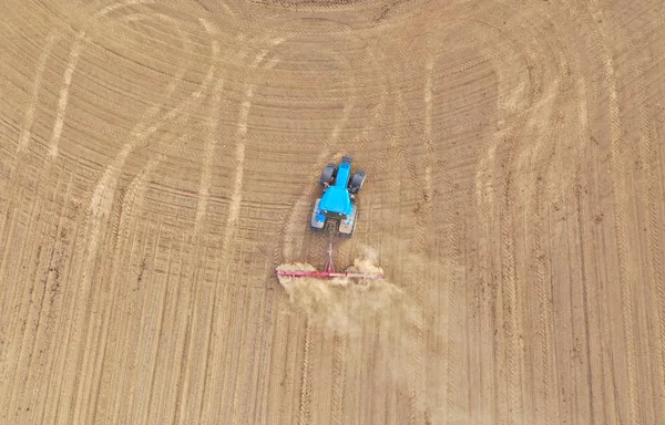 Luftaufnahme von oben auf einem blauen Traktor, der einen Pflug zieht, einen Boden für die Aussaat von Saatgut vorbereitet, Traktor macht Schmutzwolke. — Stockfoto
