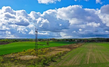 Ev, orman, bulutlar, alanlar ve elektrik güç hattı kulesi ile kırsal peyzaj havadan perspektif görünümü