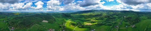 Aerial wide panoramic view on sudety mountains with touristic city in the valley surrounded by meadows, forest and rapeseed fields. — Stock Photo, Image