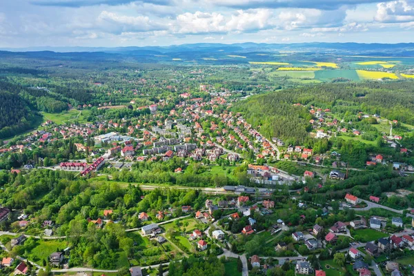 Flygperspektiv Visa på sudety Mountains med turistiska staden i dalen omgiven av ängar, skog och rapsfält. — Stockfoto