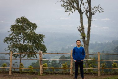 Mutlu bir adam Umbul Sidomukti, Semarang, Endonezya üzerinde arka planda sisli manzara ile poz