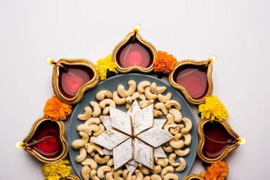 Diwali gıda Rangoli Kaju Katli tatlı kil diya/lamba ve kadife çiçeği çiçek ile birlikte kullanarak dairesel desende, seçici odak düzenlenmiştir.