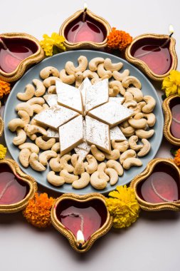 Diwali gıda Rangoli Kaju Katli tatlı kil diya/lamba ve kadife çiçeği çiçek ile birlikte kullanarak dairesel desende, seçici odak düzenlenmiştir.