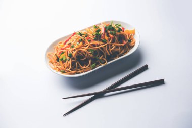 Schezwan erişte veya sebze Hakka erişte veya chow mein tahta çubukla bir kase veya plaka servis popüler Hint-Çin yemek tarifleri, var. seçici odak