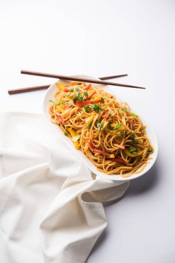 Schezwan Noodles or vegetable Hakka Noodles or chow mein is a popular Indo-Chinese recipes, served in a bowl or plate with wooden chopsticks. selective focus clipart